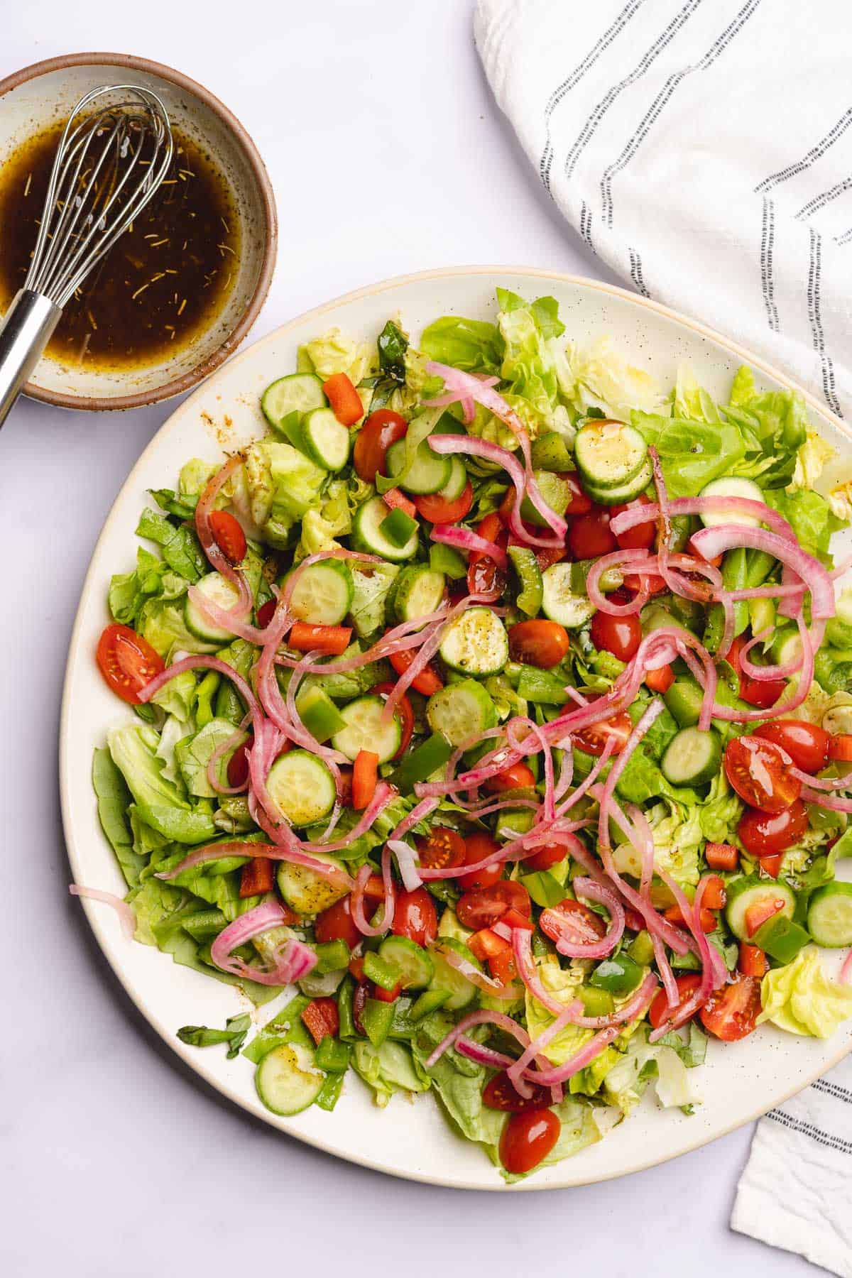 building a keto antipasto salad with tomatoes, cucumbers and pickled red onions on a bed of lettuce