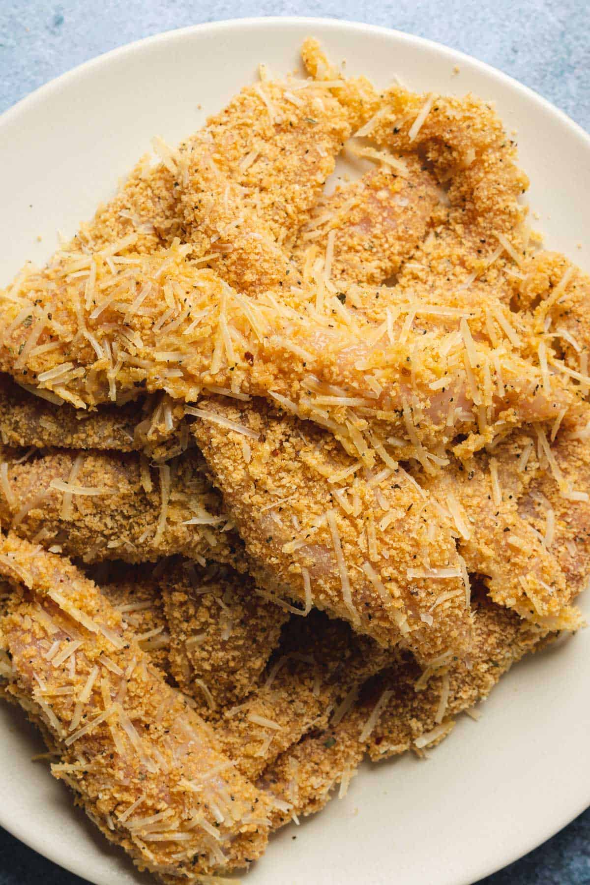chicken coated in pork rinds and shredded parmesan ready to be fried 