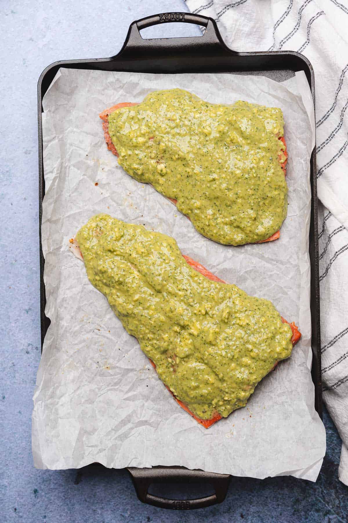 raw salmon fillets covered in pesto butter mixture on a prepared baking sheet