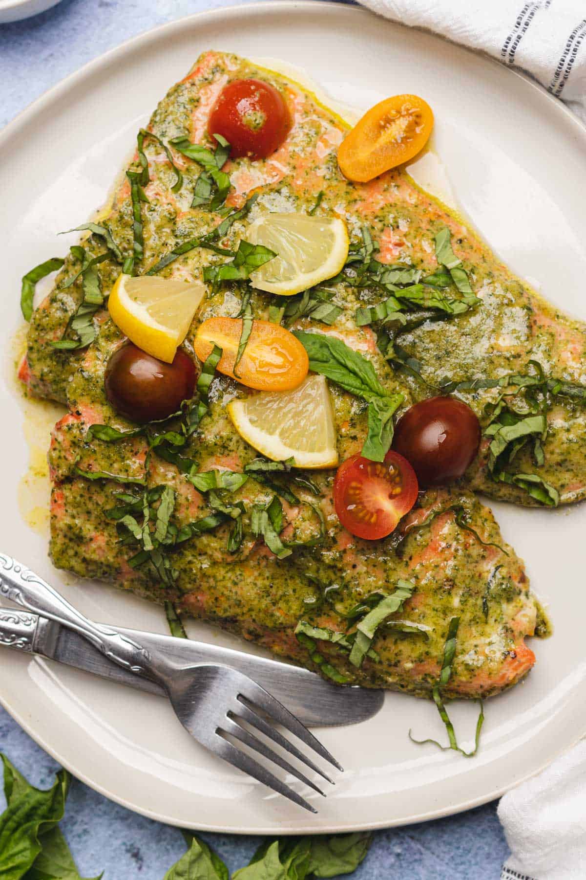 two pieces of pesto butter salmon with tomatoes and lemon
