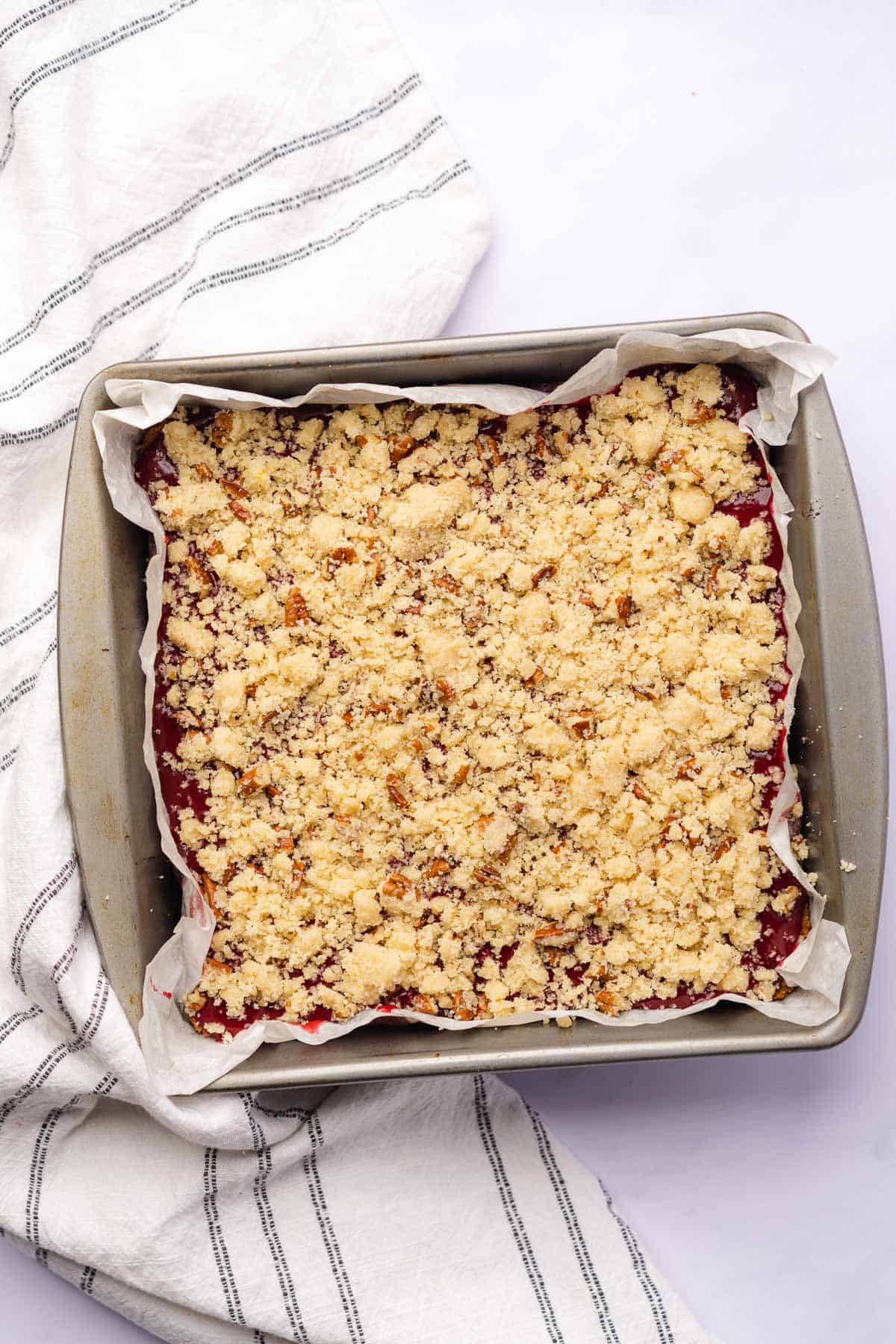 plum bars with pecan crumble topping raw in a 9x9 baking pan with white parchment