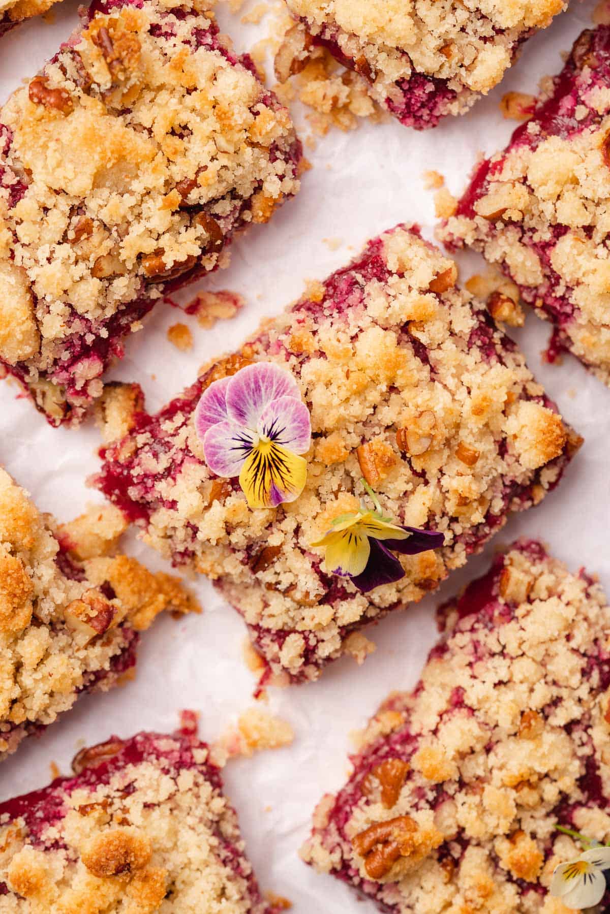 flat lay of plum crumble bars with an edible flower on top on white parchment 