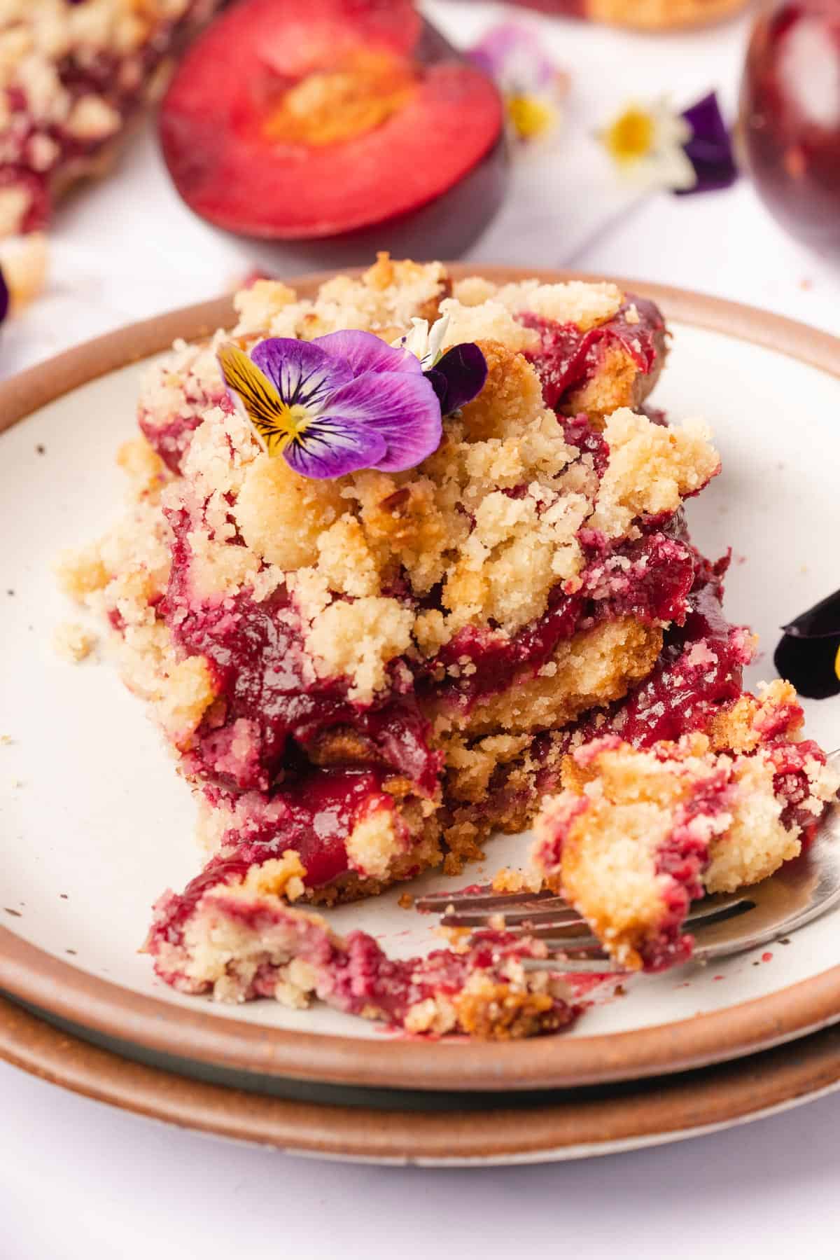 stack of plum crumble bars with a bite taken out with edible flowers on top