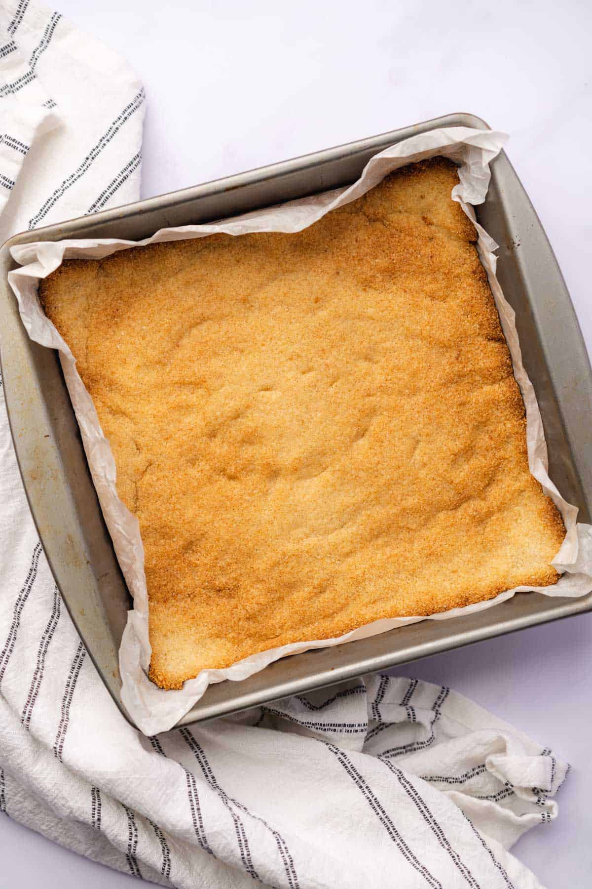 baked gluten free almond flour shortbread crust in a 9x9 pan with white parchment paper 