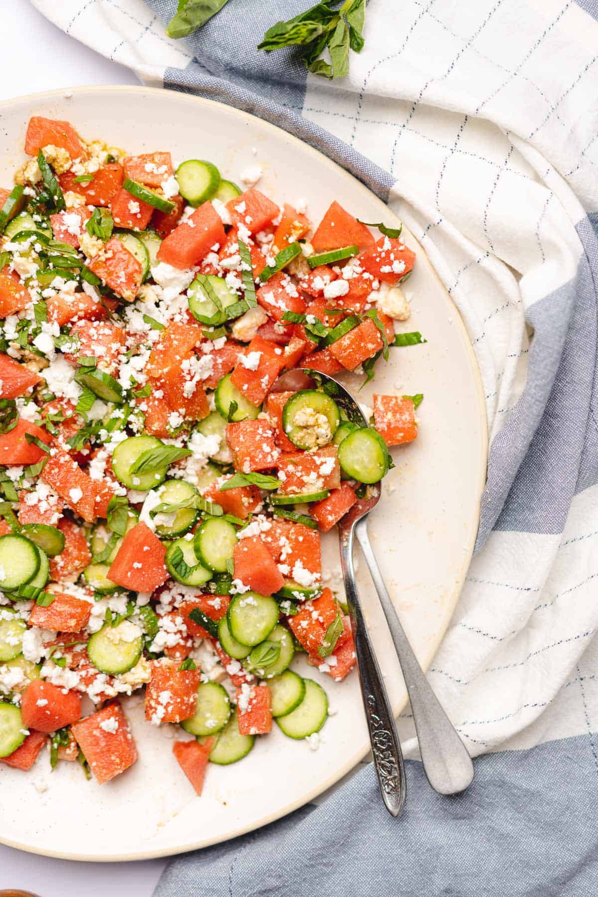 spoon tucked into the side of a watermelon feta salad with herbs and cucumber