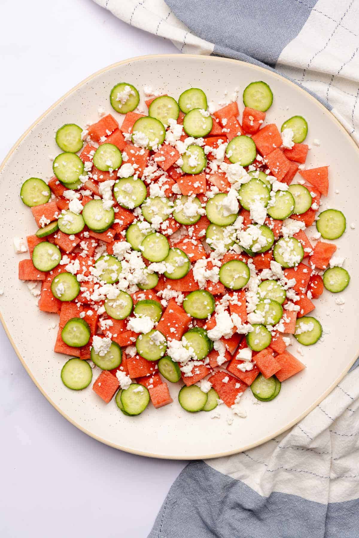 adding feta cheese to watermelon and feta on a large serving platter