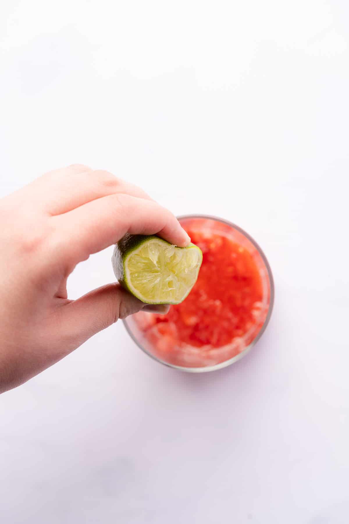 hand squeezing fresh lime juice into the bottom of a cocktail 