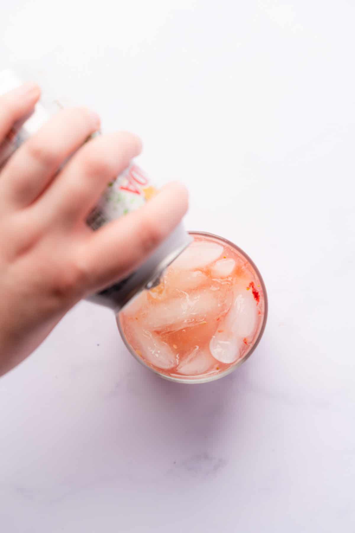 hand pouring diet ginger ale into a pink cocktail with ice 