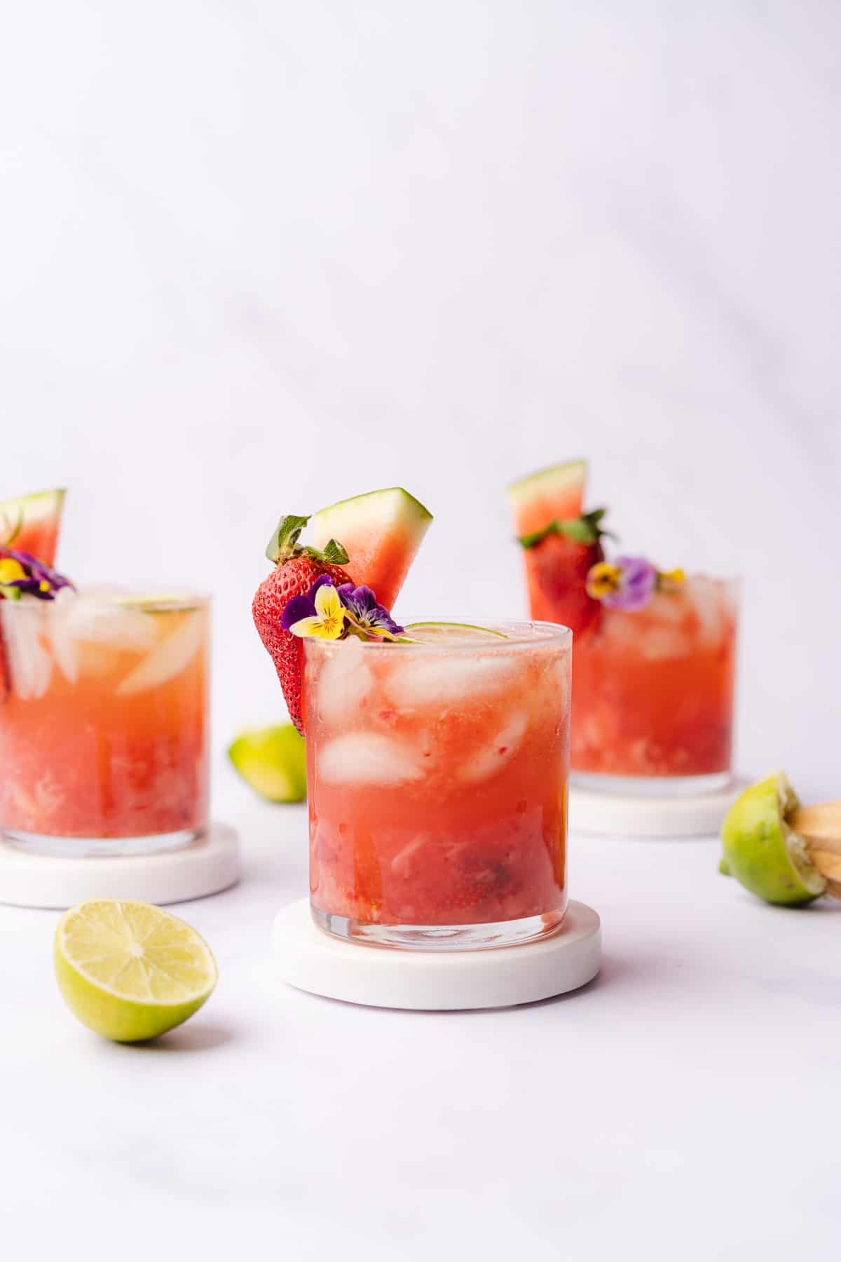 3 classes of watermelon wine spritzers with chunks of watermelon, juiced limes and edible flowers