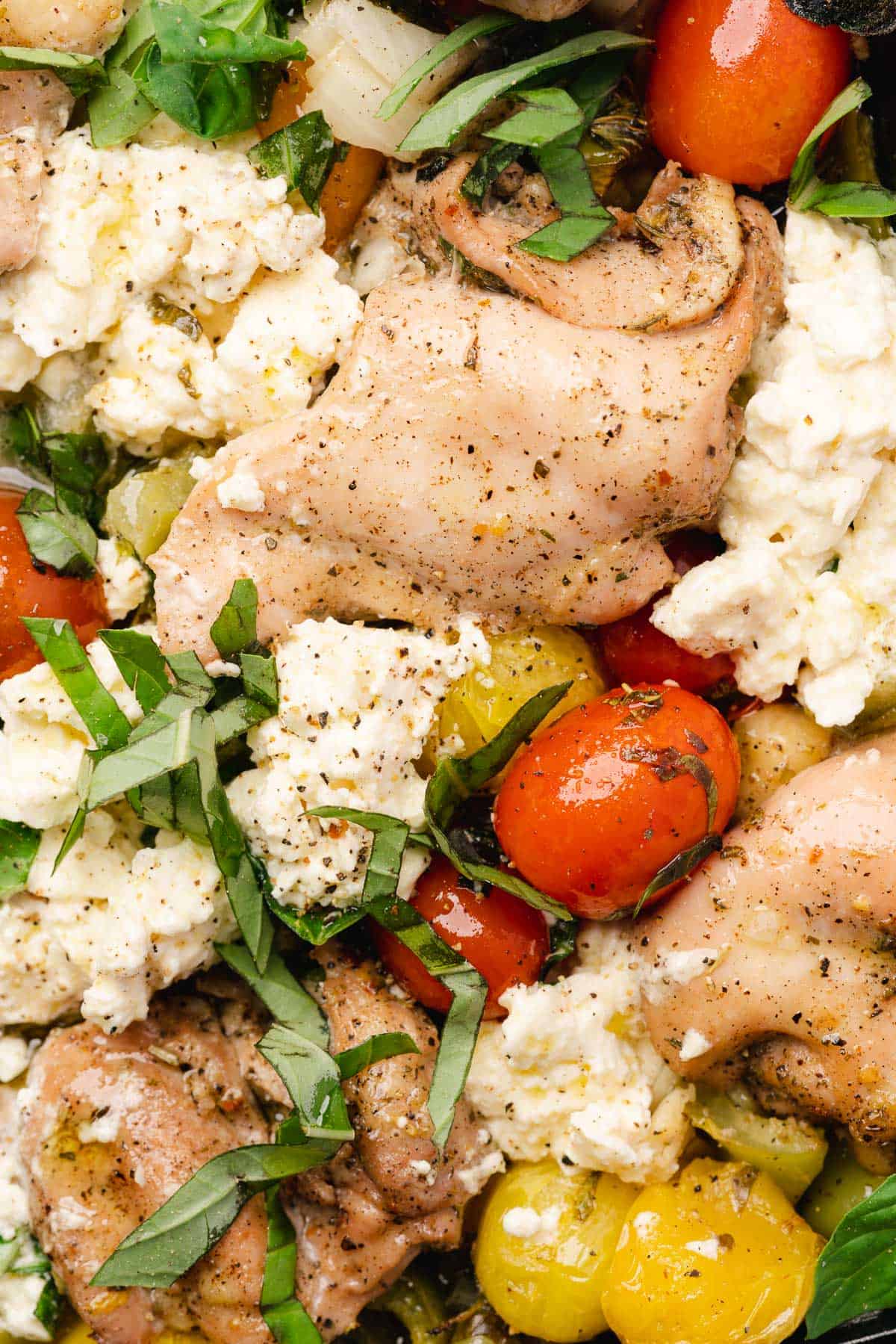 close up shot of a chicken thigh with feta and tomatoes 