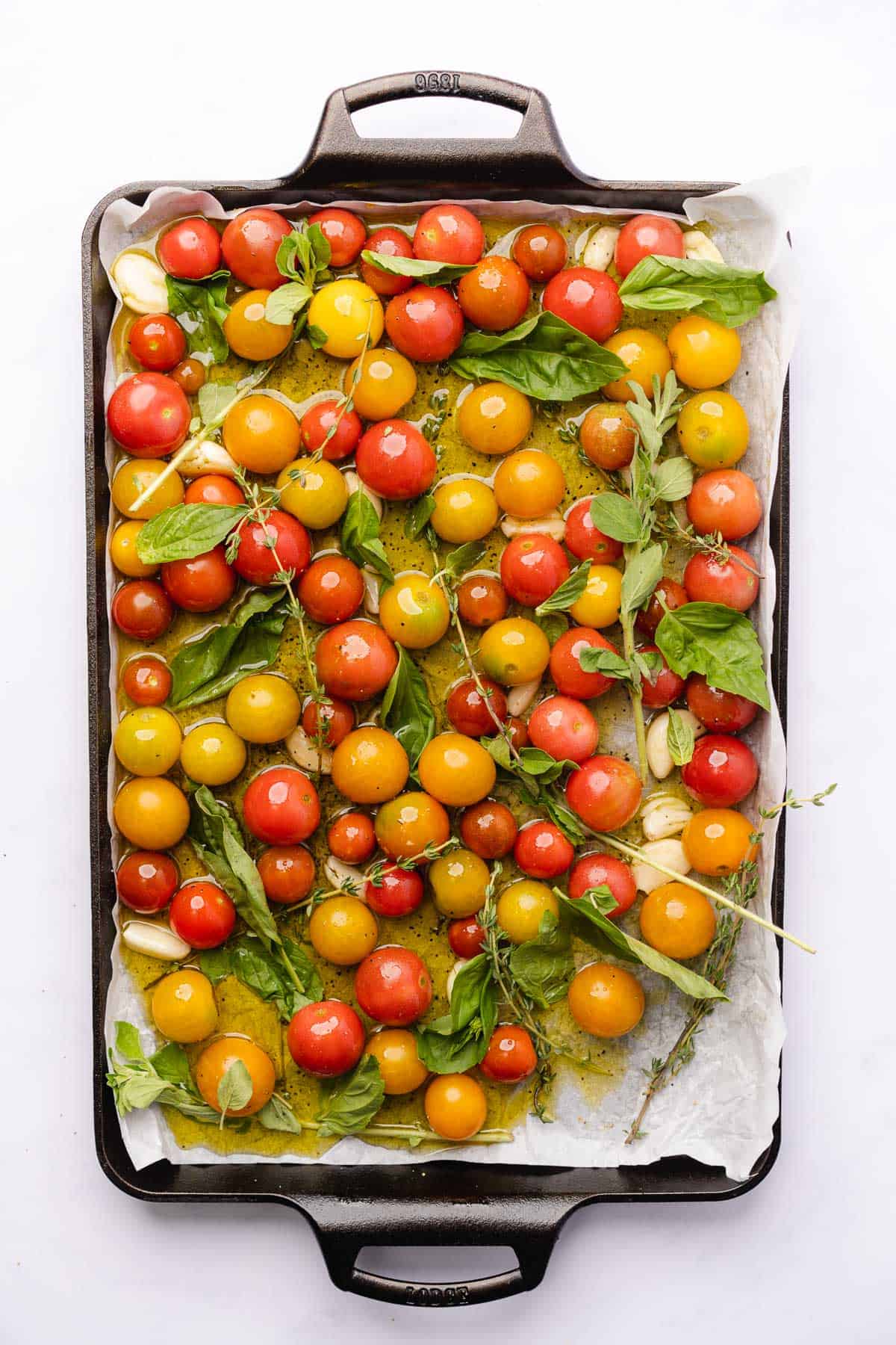 fresh herbs over top of cherry tomato confit ingredients on a baking sheet
