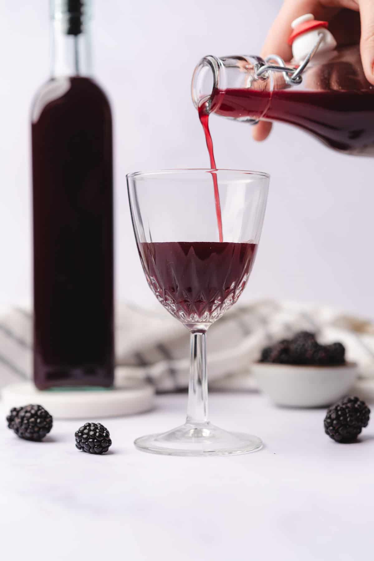 pouring creme de mure blackberry liqueur into a small wine glass