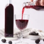 lovely handheld shot of pouring creme de mure blackberry liqueur into a wine glass