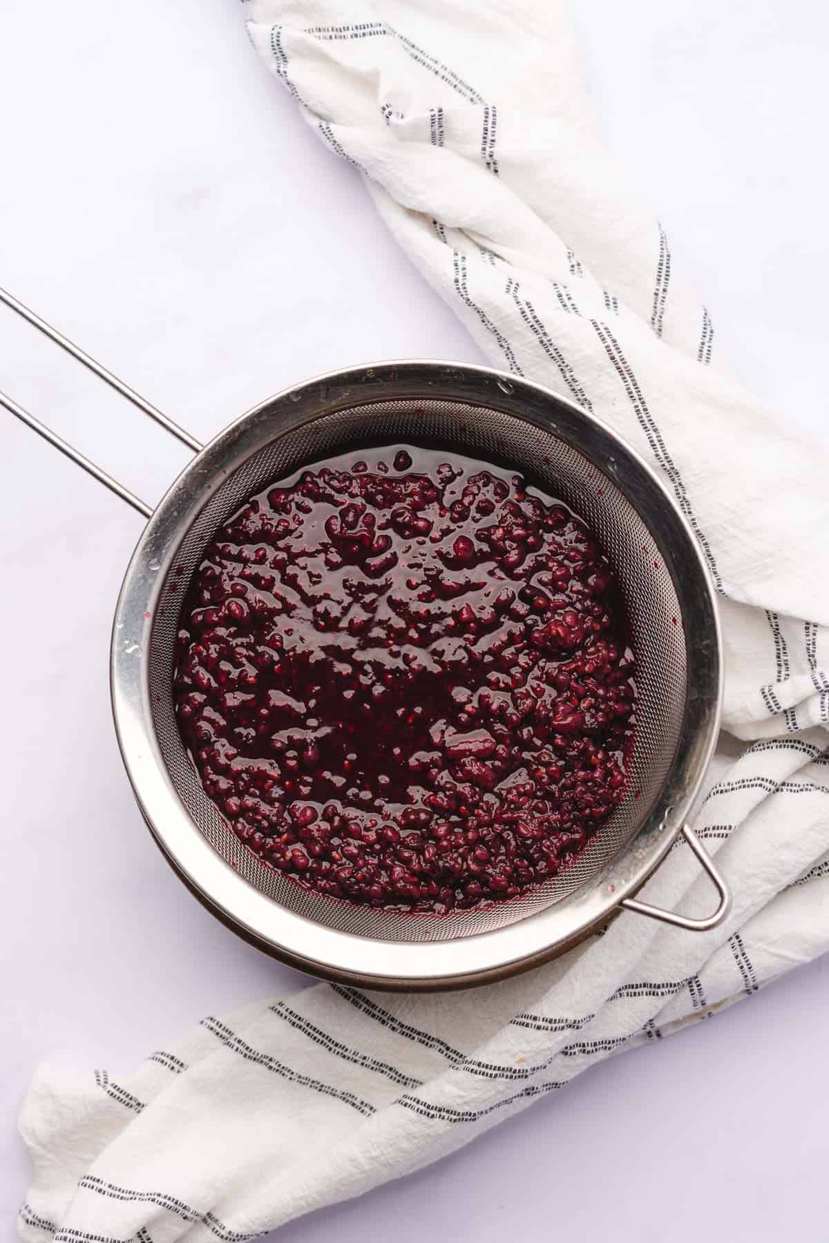 straining blackberries away from red wine using a metal sieve 