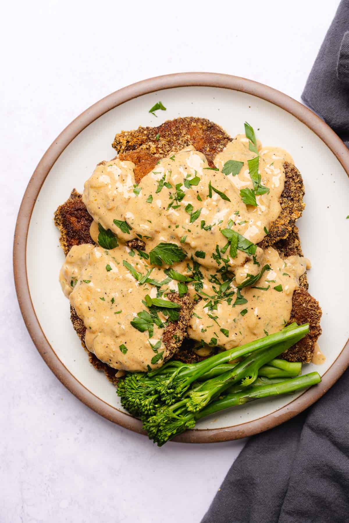 plate of pork chops and gravy with a side of steamed broccolini 