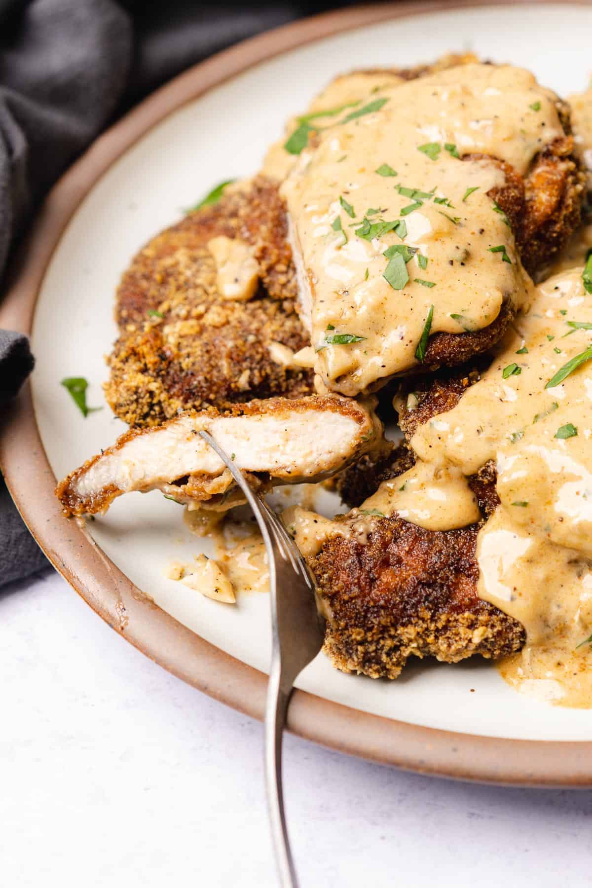 plate of keto fried pork chops smothered in southern gravy with a forkful showing the inside of the pork chop