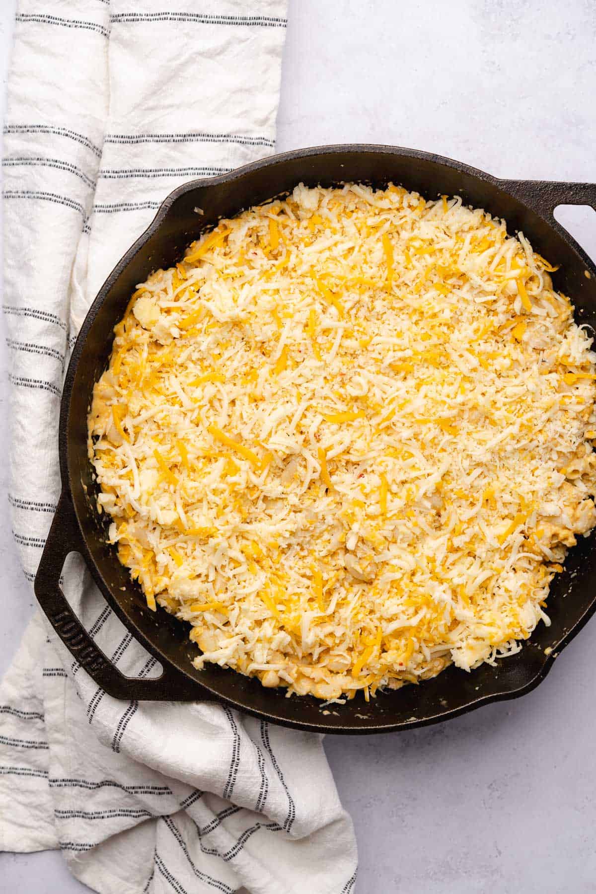 macaroni with cheese on top in a cast iron skillet getting ready to bake