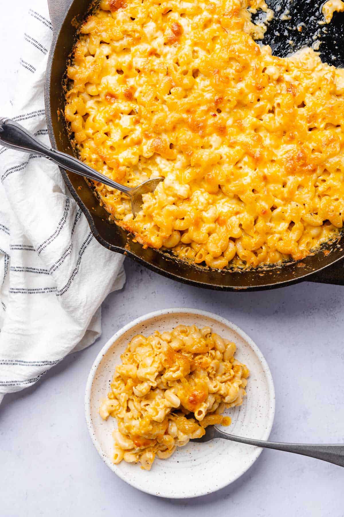 cast iron skillet with mac and cheese besides a small plate serving of mac and cheese