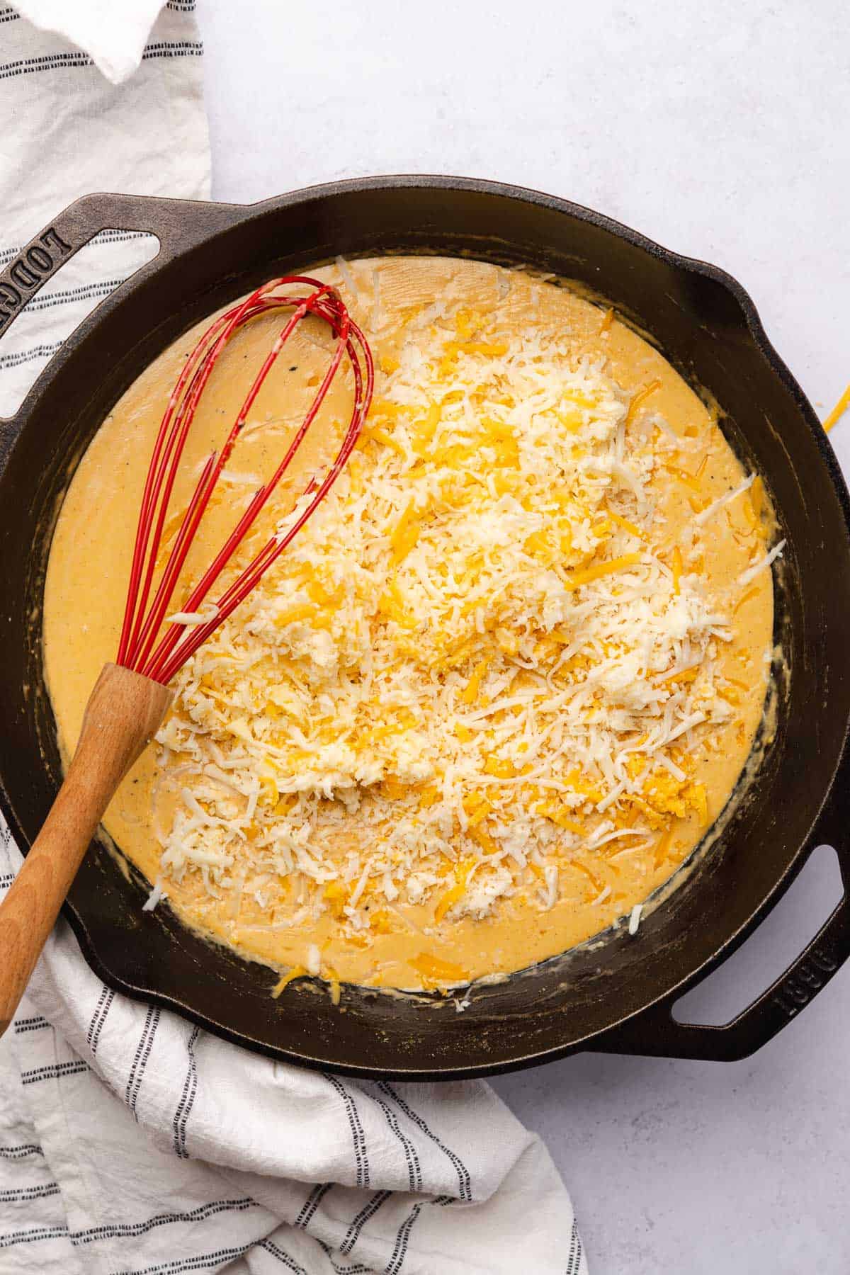 adding cheddar and pepper jack cheese to make a keto cheese sauce in a cast iron skillet