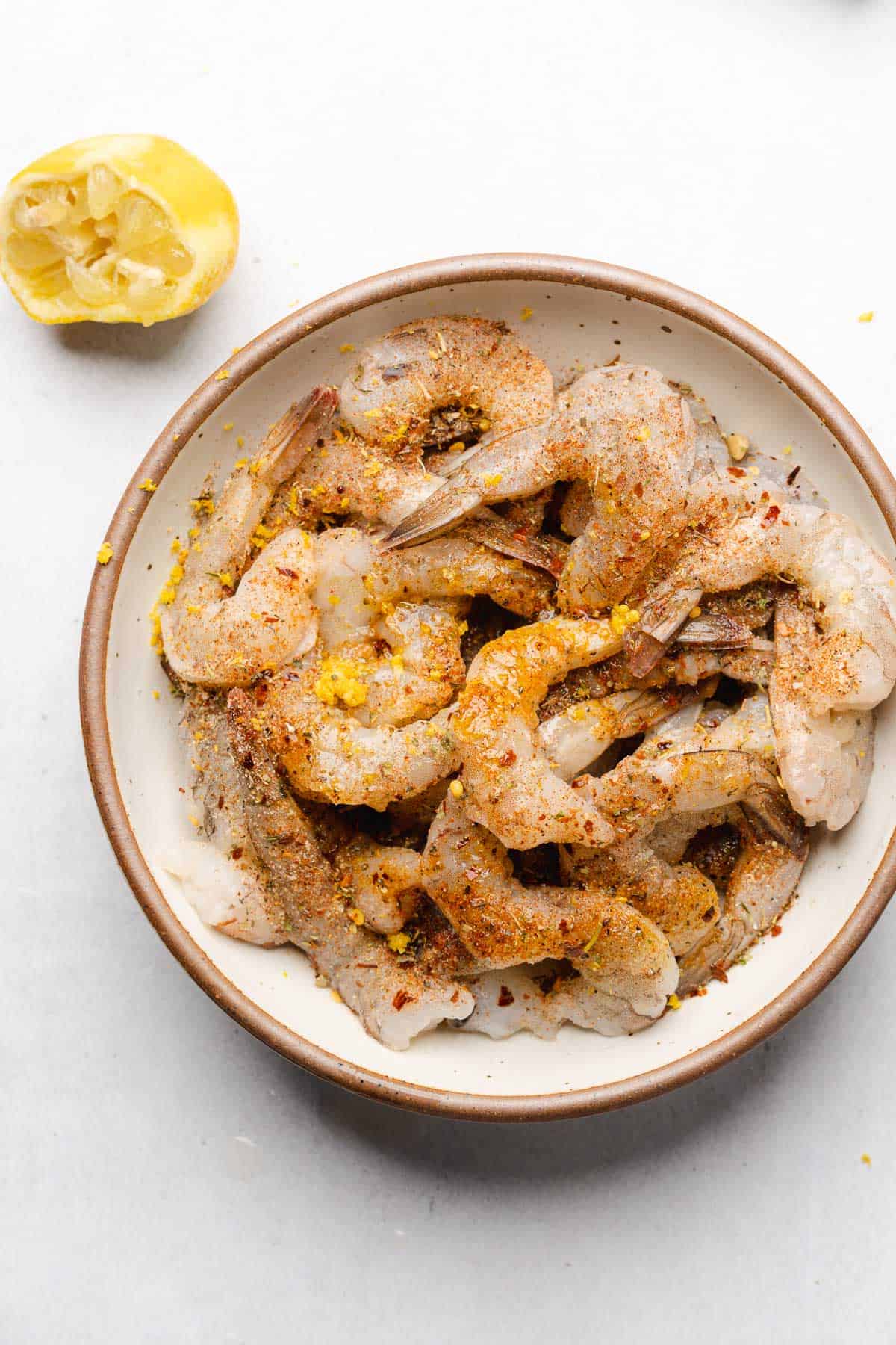 shrimp in a bowl with seasonings, olive oil and lemon juice and zest