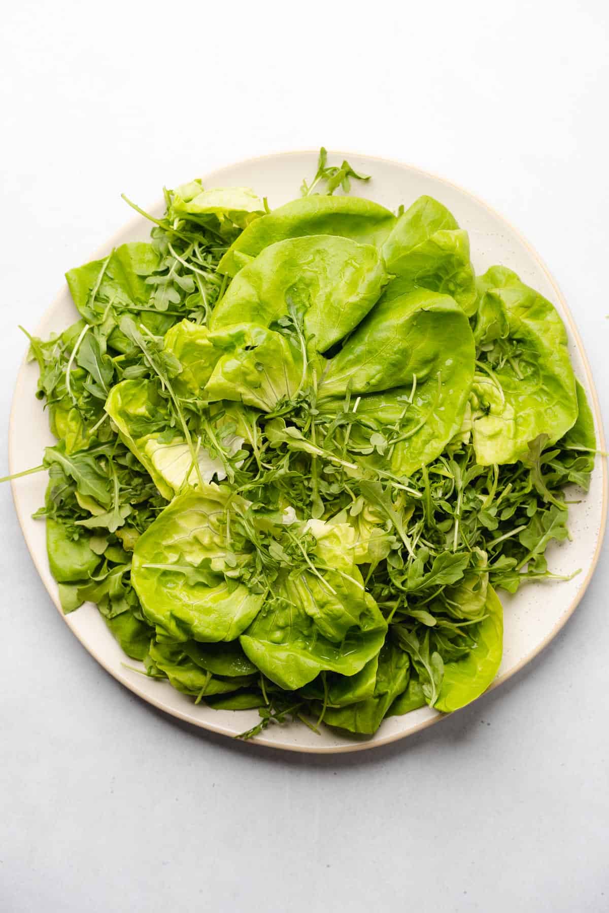 butter lettuce and arugula on a serving plate to make a salad
