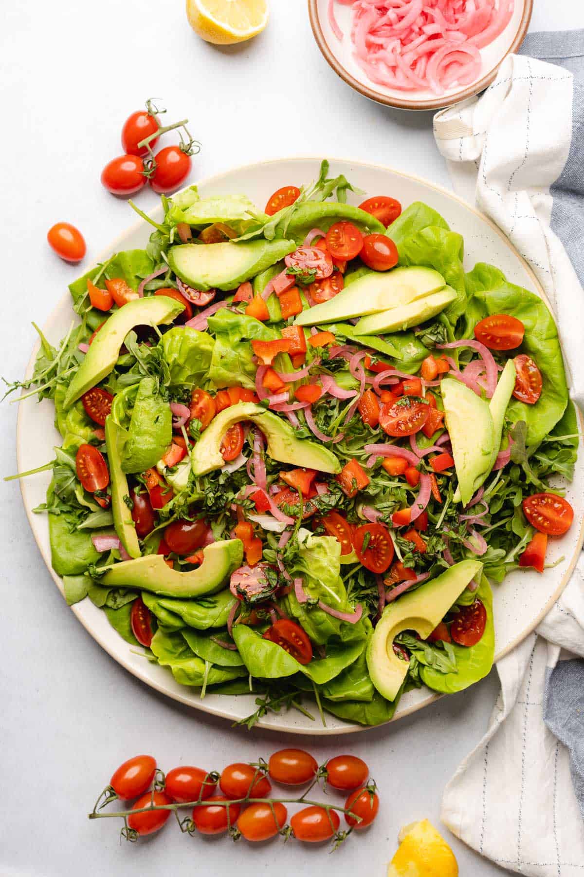 bed of lettuce and arugula with pickled red onions, avocado, red bell peppers and tomatoes on top