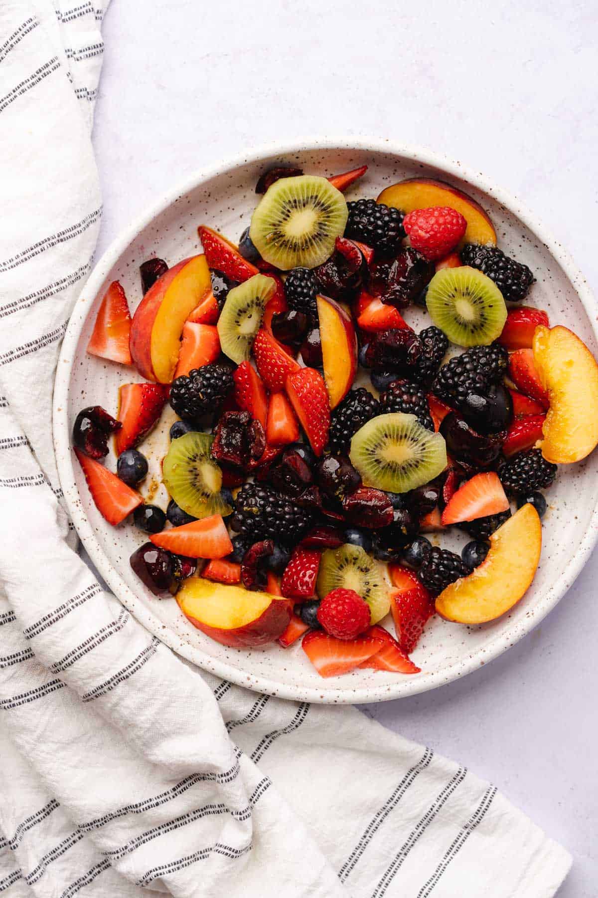 fruit salad with peaches, berries and kiwi on a large white ceramic serving platter