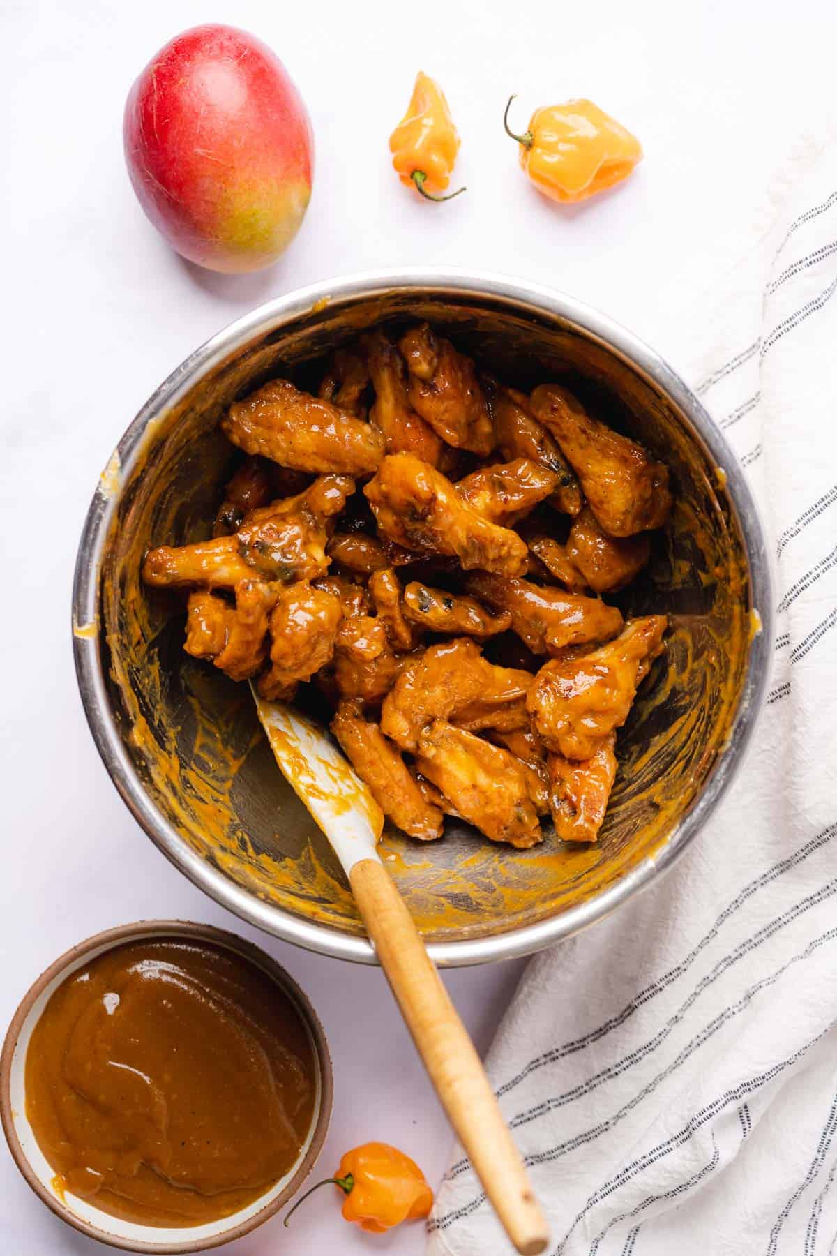 coating chicken wings in mango sauce in a bowl with a rubber spatula 