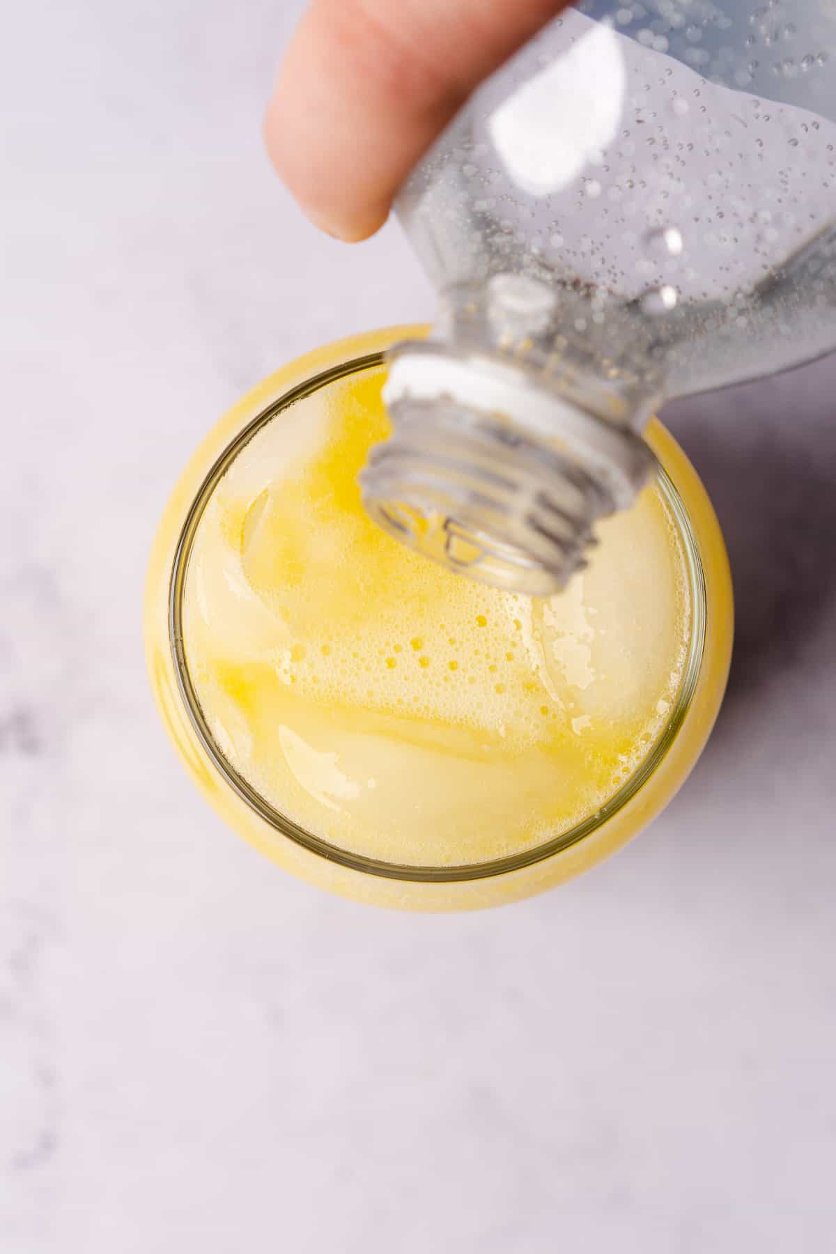 pouring in club soda to a mango mojito in a glass