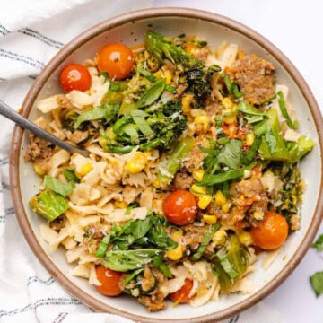 sausage broccolini pasta with corn and tomatoes in a ceramic bowl with parmesan cheese