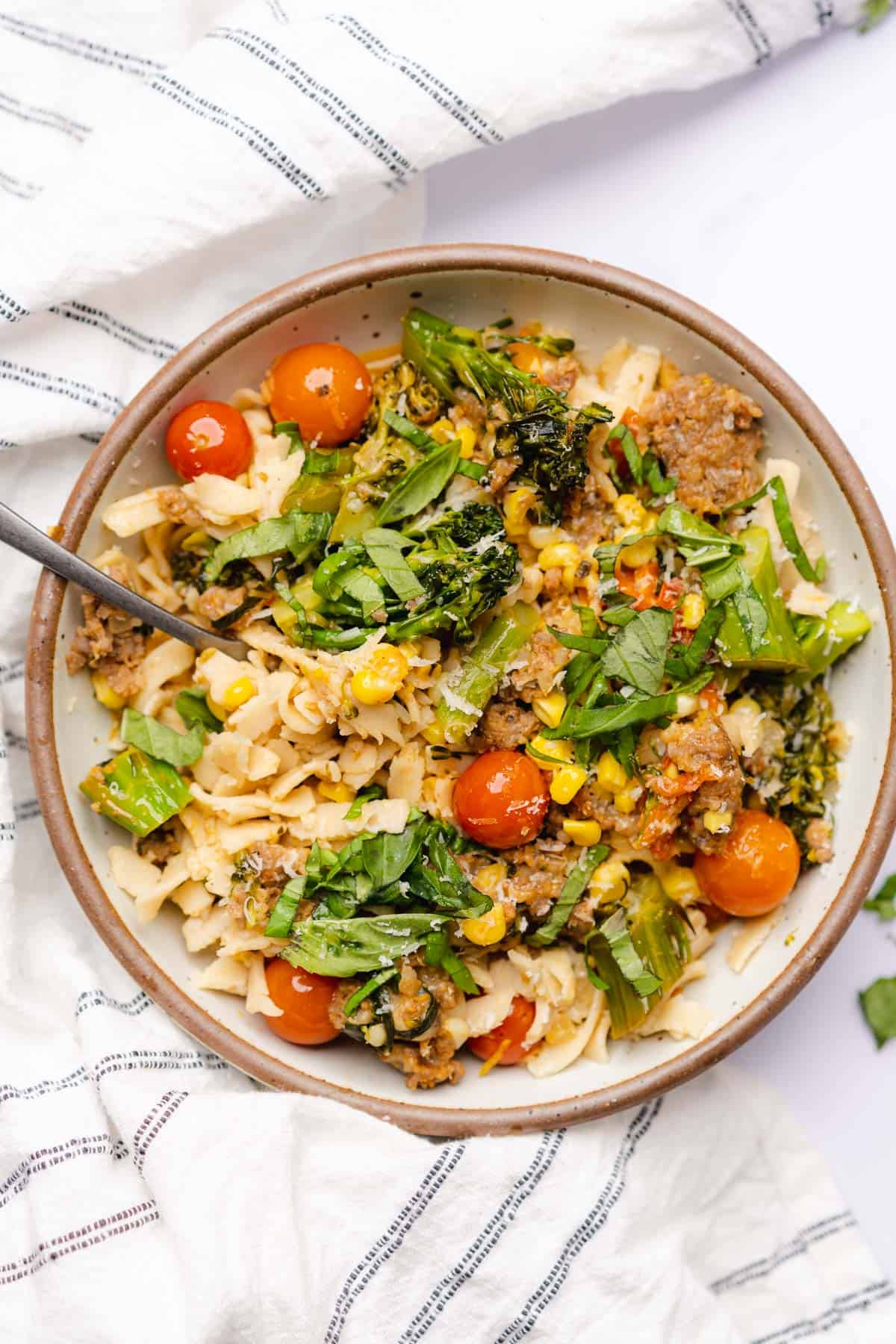 sausage broccolini pasta with corn and tomatoes in a ceramic bowl with parmesan cheese