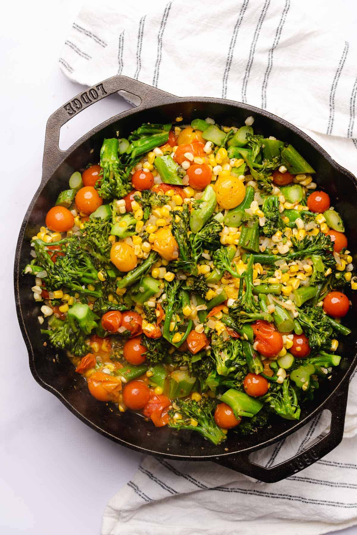 cooked broccolini, corn and tomatoes in a cast iron skillet