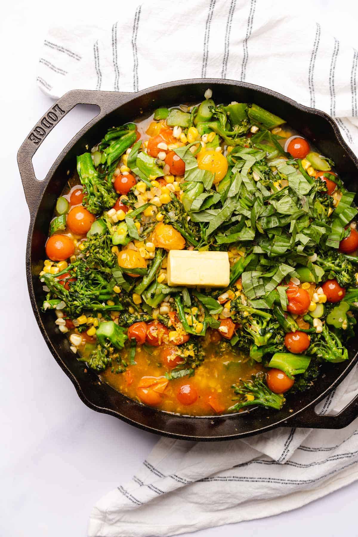 bright broccolini, corn and tomatoes with butter and chicken broth in a cast iron skillet