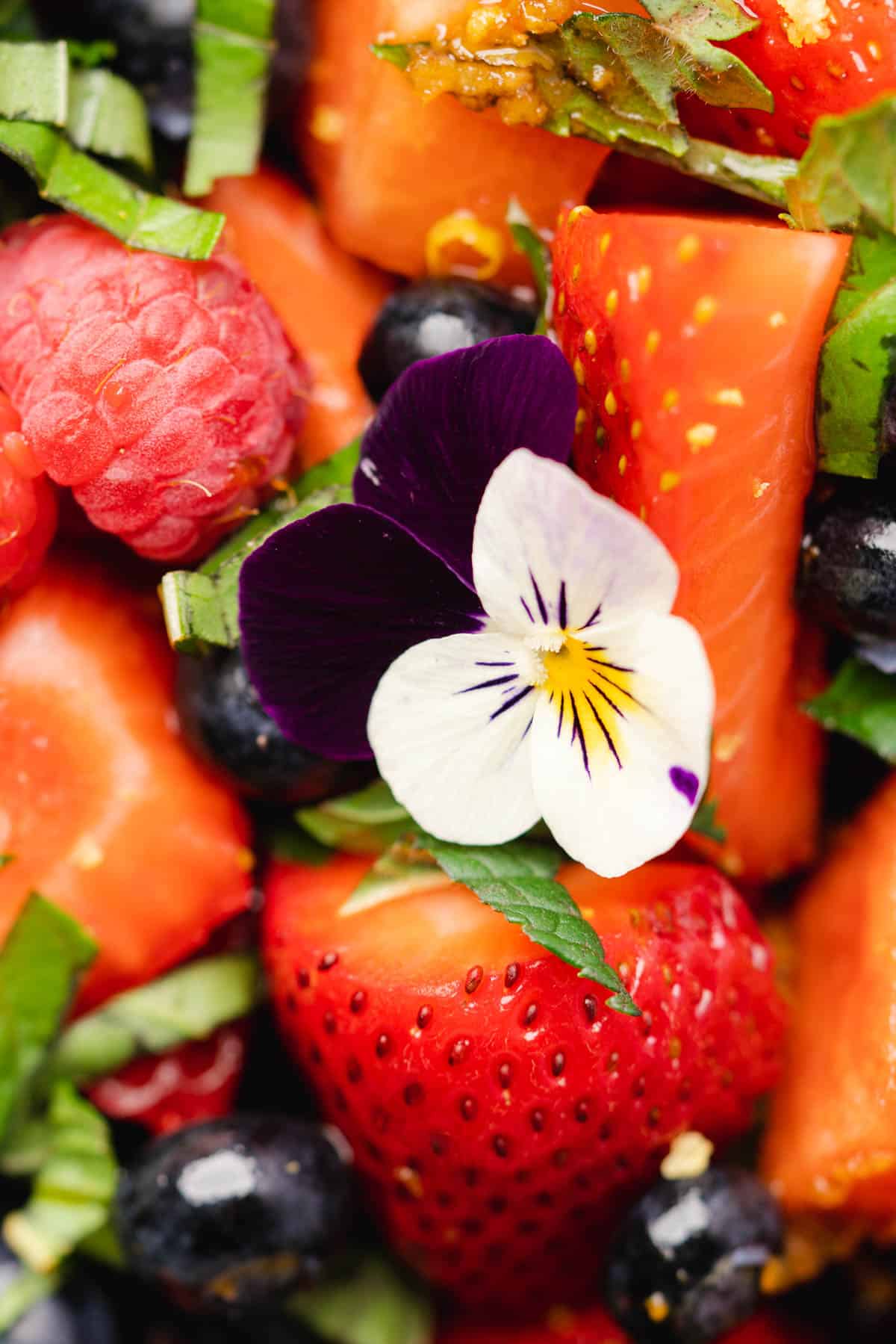 close up shot of watermelon and berries  with basil ribbons and edible flowers