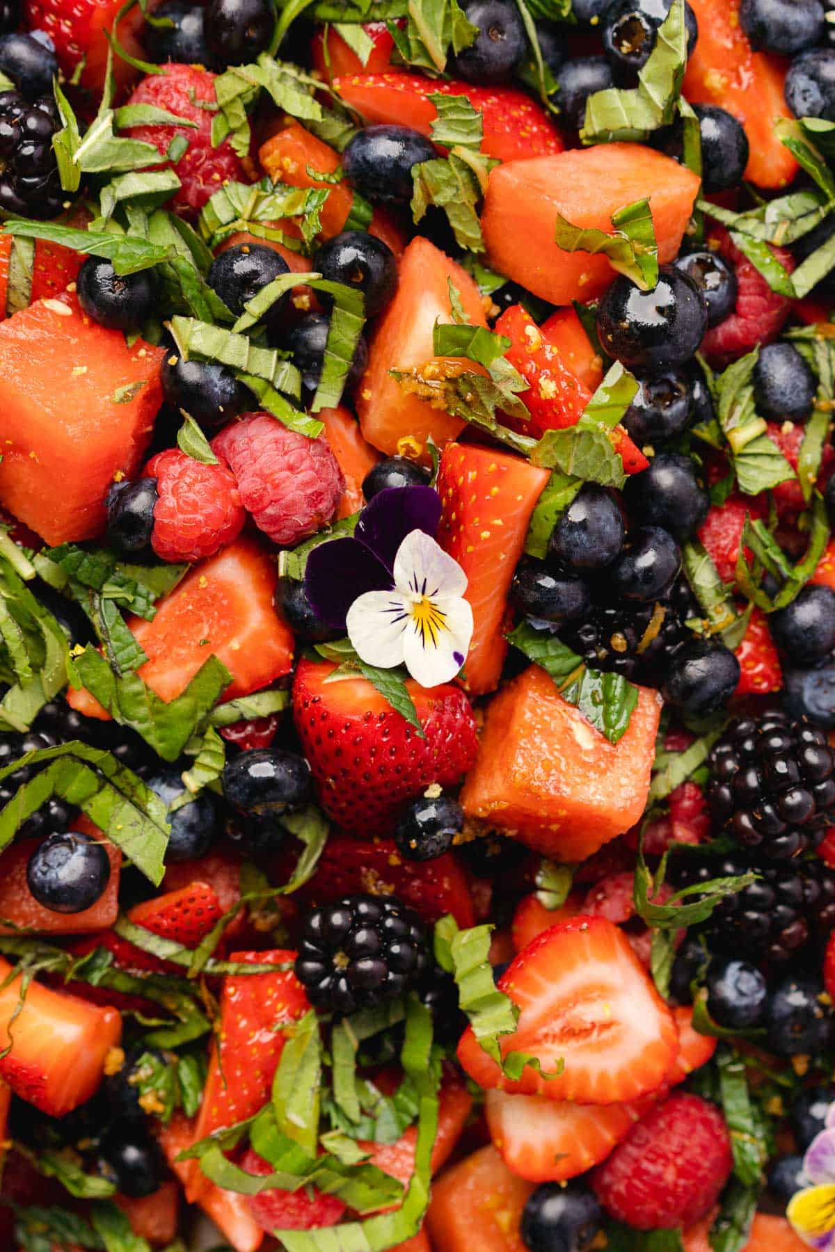 close up shot of watermelon with blackberries, blueberries, raspberries, strawberries, basil and edible flowers