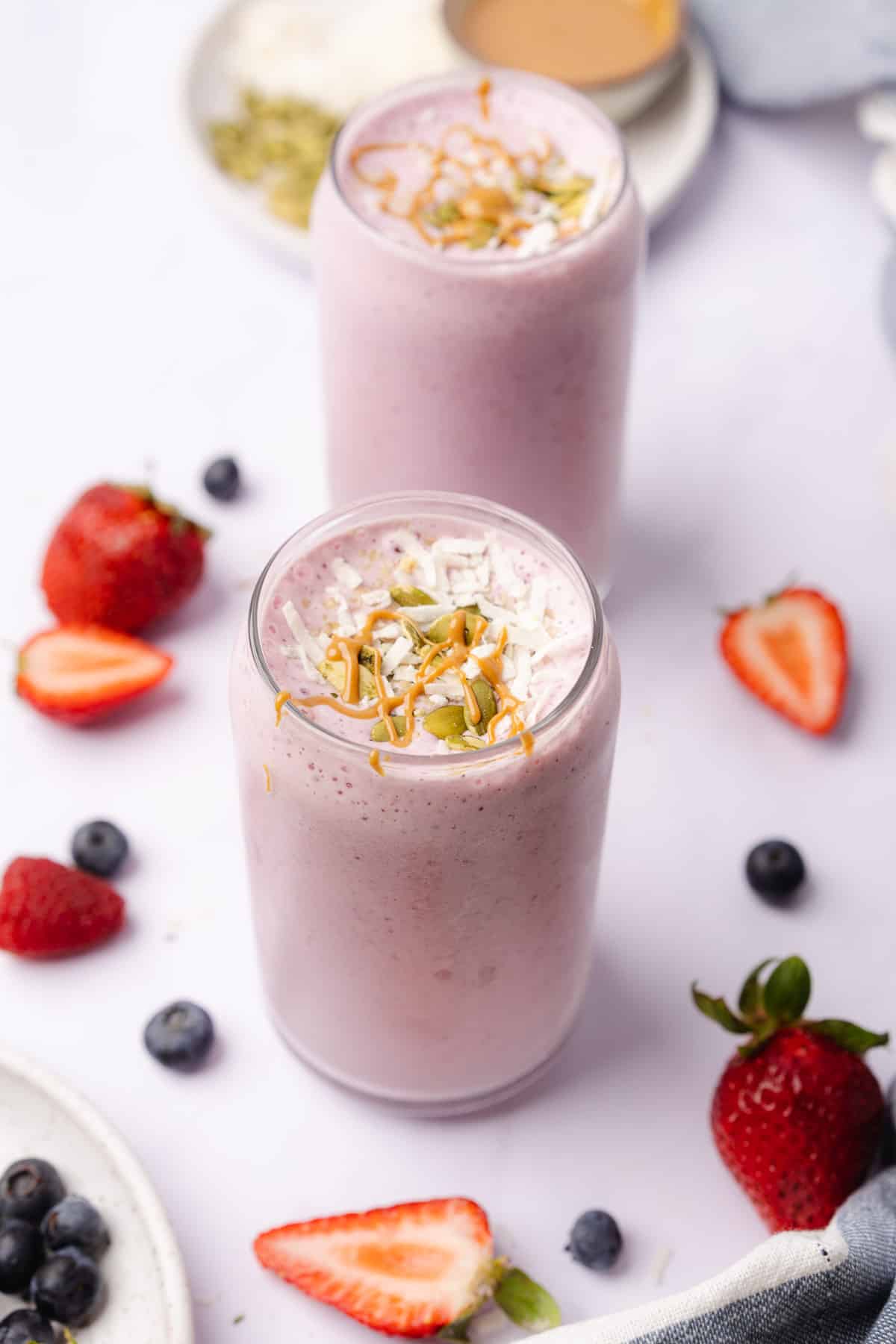 two glasses of keto berry smoothie topped with nuts and coconut toppings with fresh berries