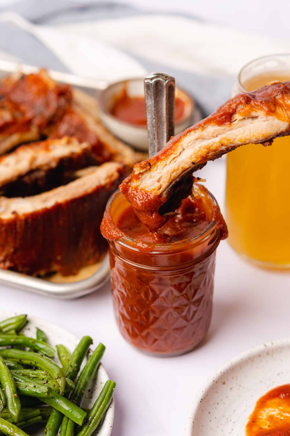 close up shot of dipping a pork rib into a jar of keto bbq sauce