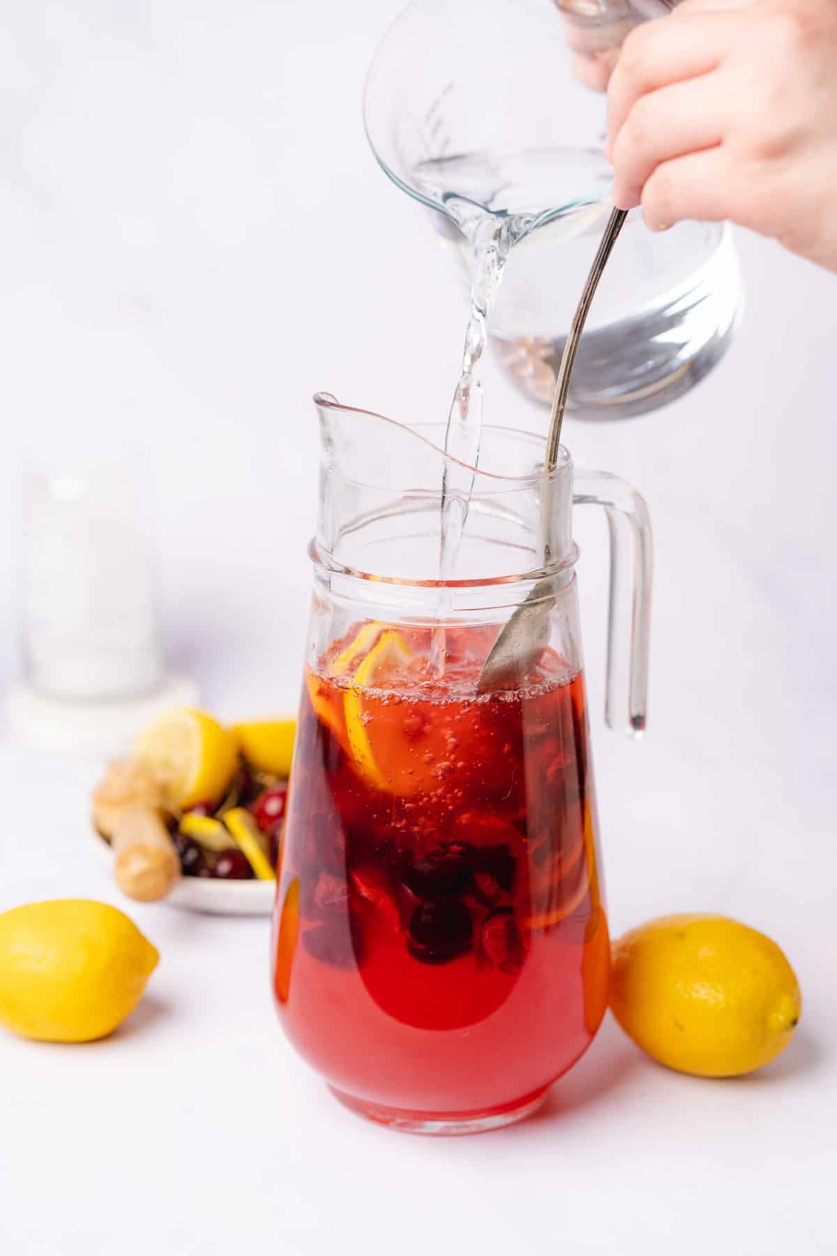 hand pouring cold water into a pitcher of cherry lemonade