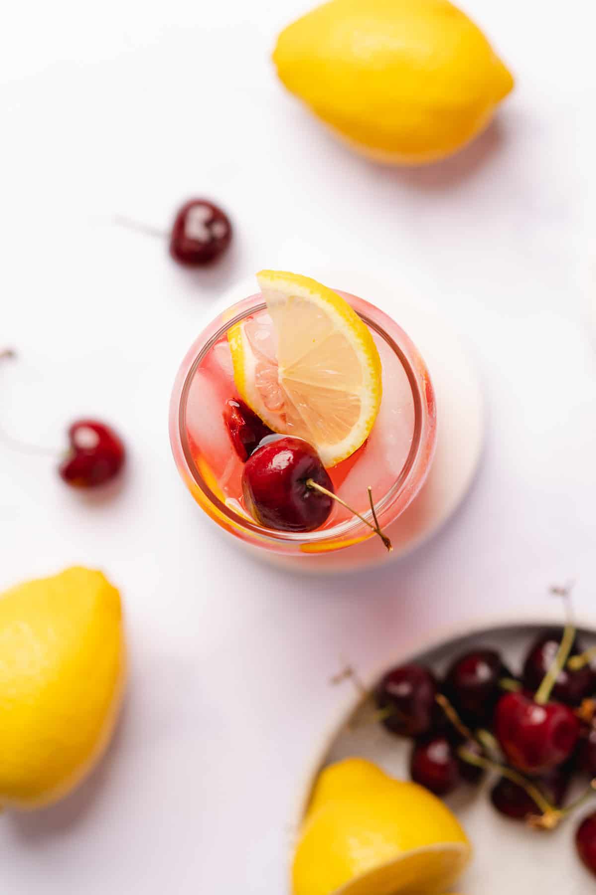 flat lay shot of cherry lemonade with a plate of cherries surrounding it