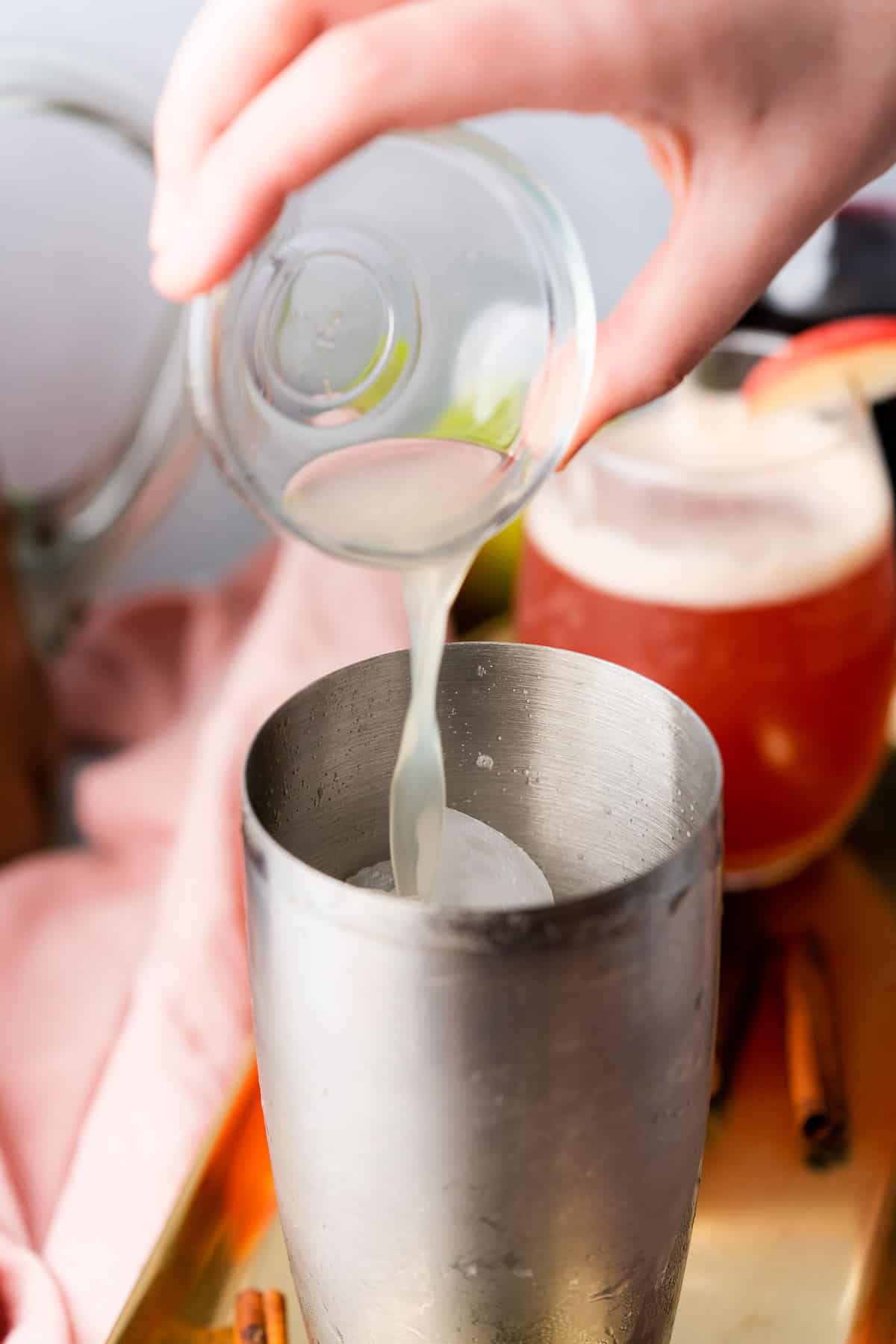 hand pouring fresh squeezed lime juice into a cocktail shaker.