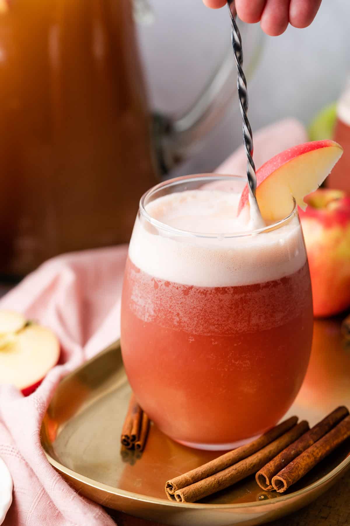 stirring an apple cider bourbon cocktail with a cocktail spoon.