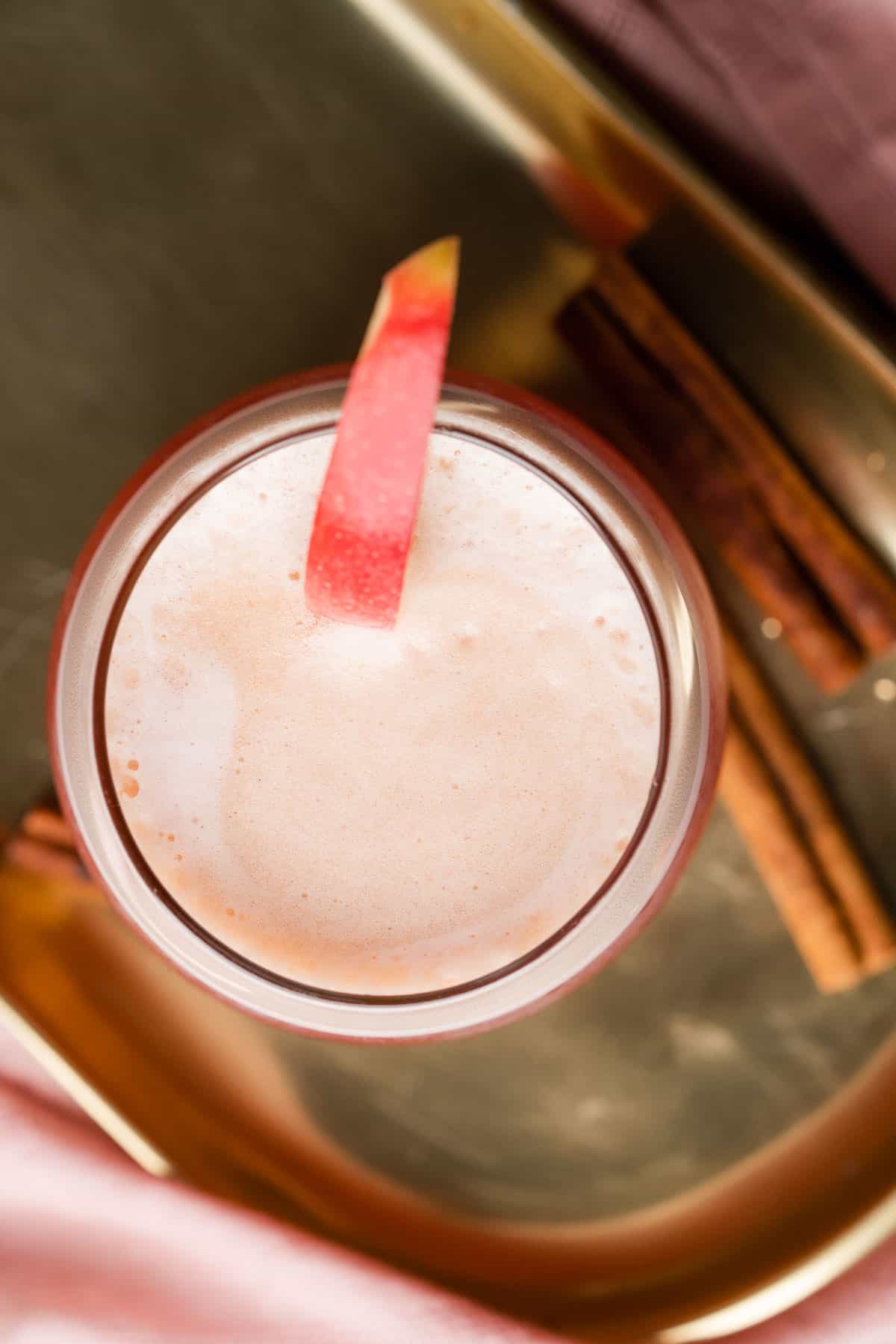 apple cider bourbon cocktail on a gold plate with cinnamon sticks and apple wedges