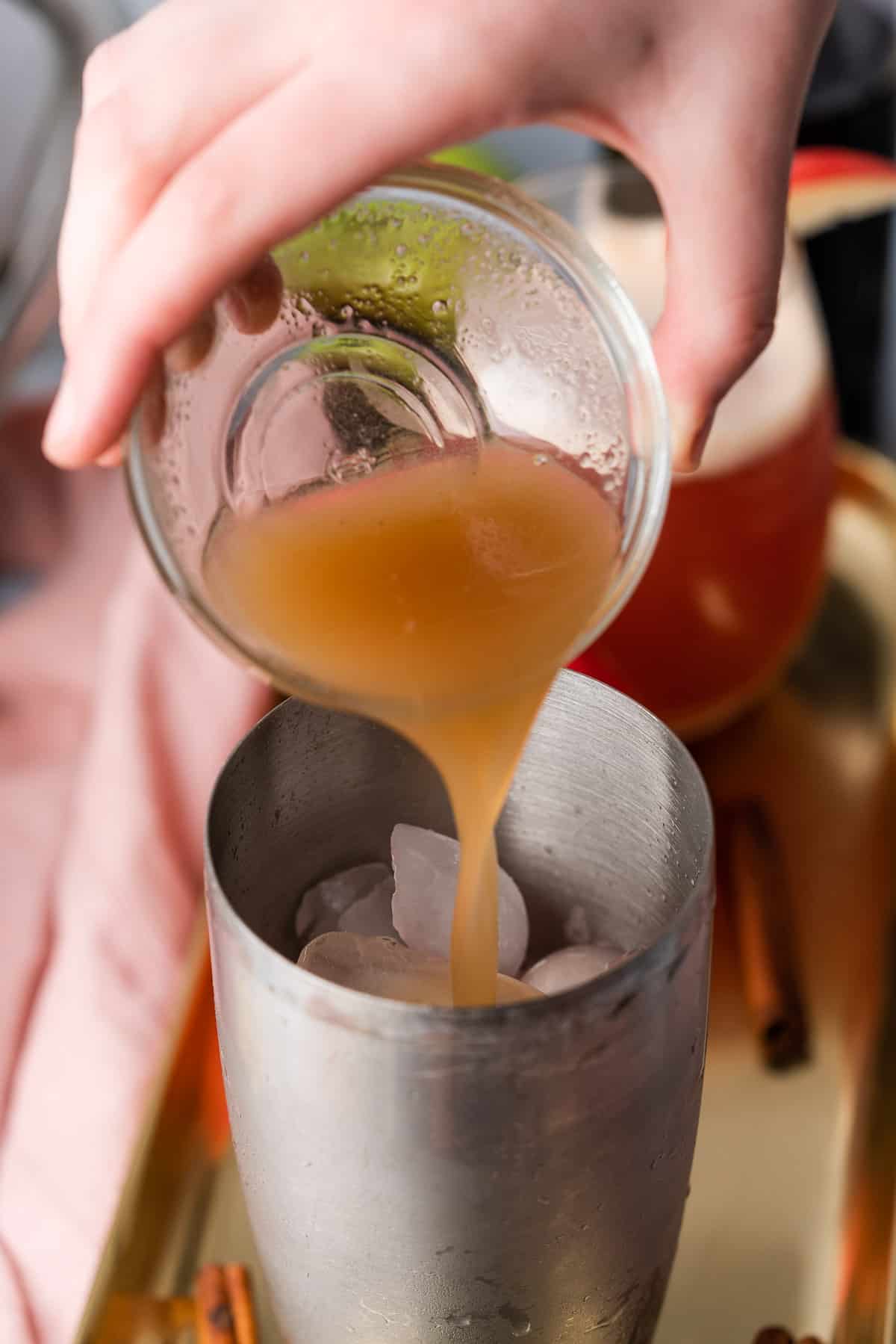 hand pouring apple cider into a cocktail shaker.