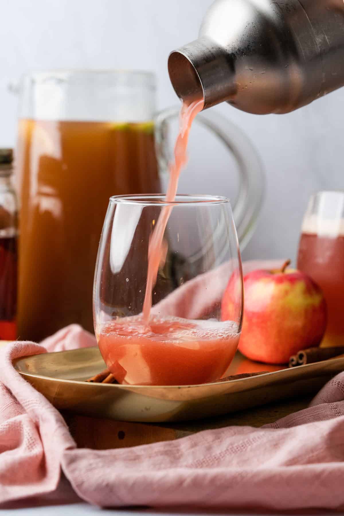 pouring apple cider bourbon cocktail in a cocktail shaker into a stemless wine glass