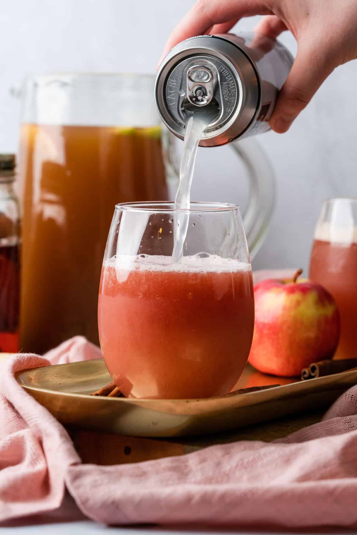 hand topping off an apple cider bourbon cocktail with ginger beer