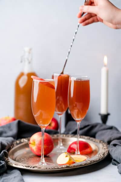 hand stirring an apple cider mimosa cocktail with a white tall candle lit in the background