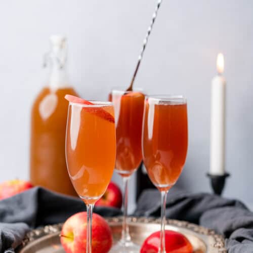 hand stirring an apple cider mimosa cocktail with a white tall candle lit in the background