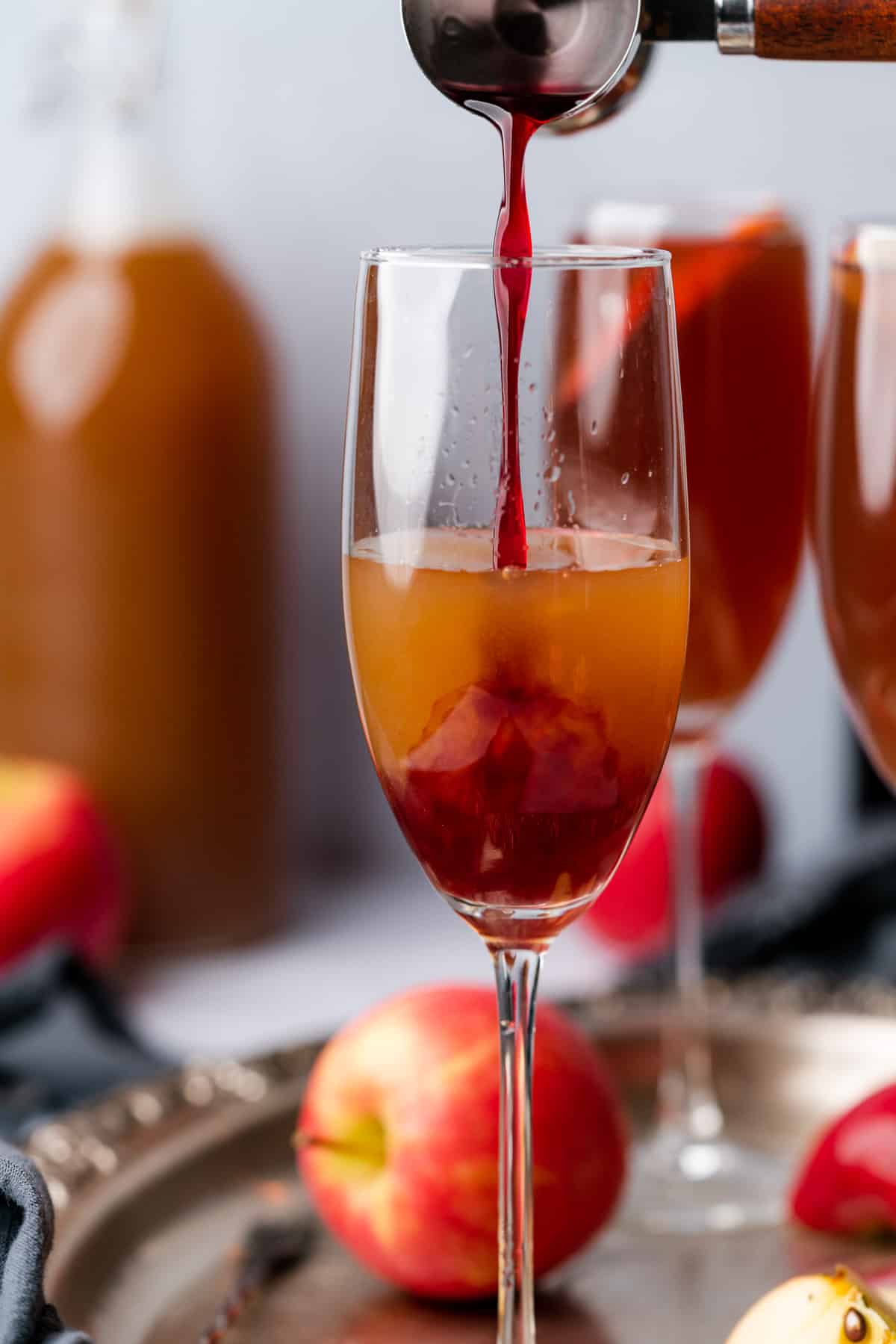 slowly pouring in homemade grenadine to an apple cider cocktail in a champagne flute