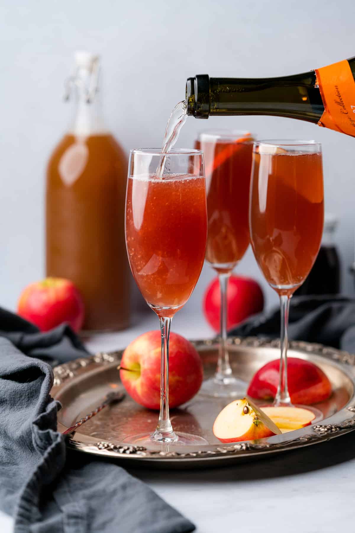 pouring prosecco into some tall champagne flutes surrounded by apples