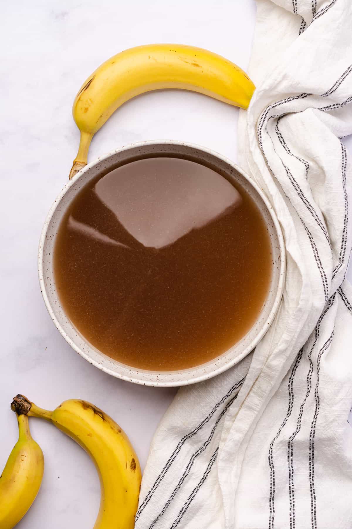 banana liqueur in a ceramic bowl surrounded by a linen napkin and bananas 